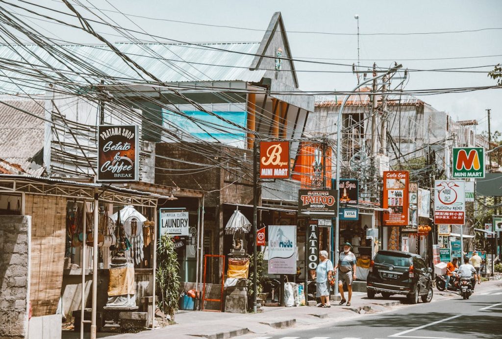 Lively urban street scene with busy shops and overhead cables on a sunny day, vibrant with local culture.